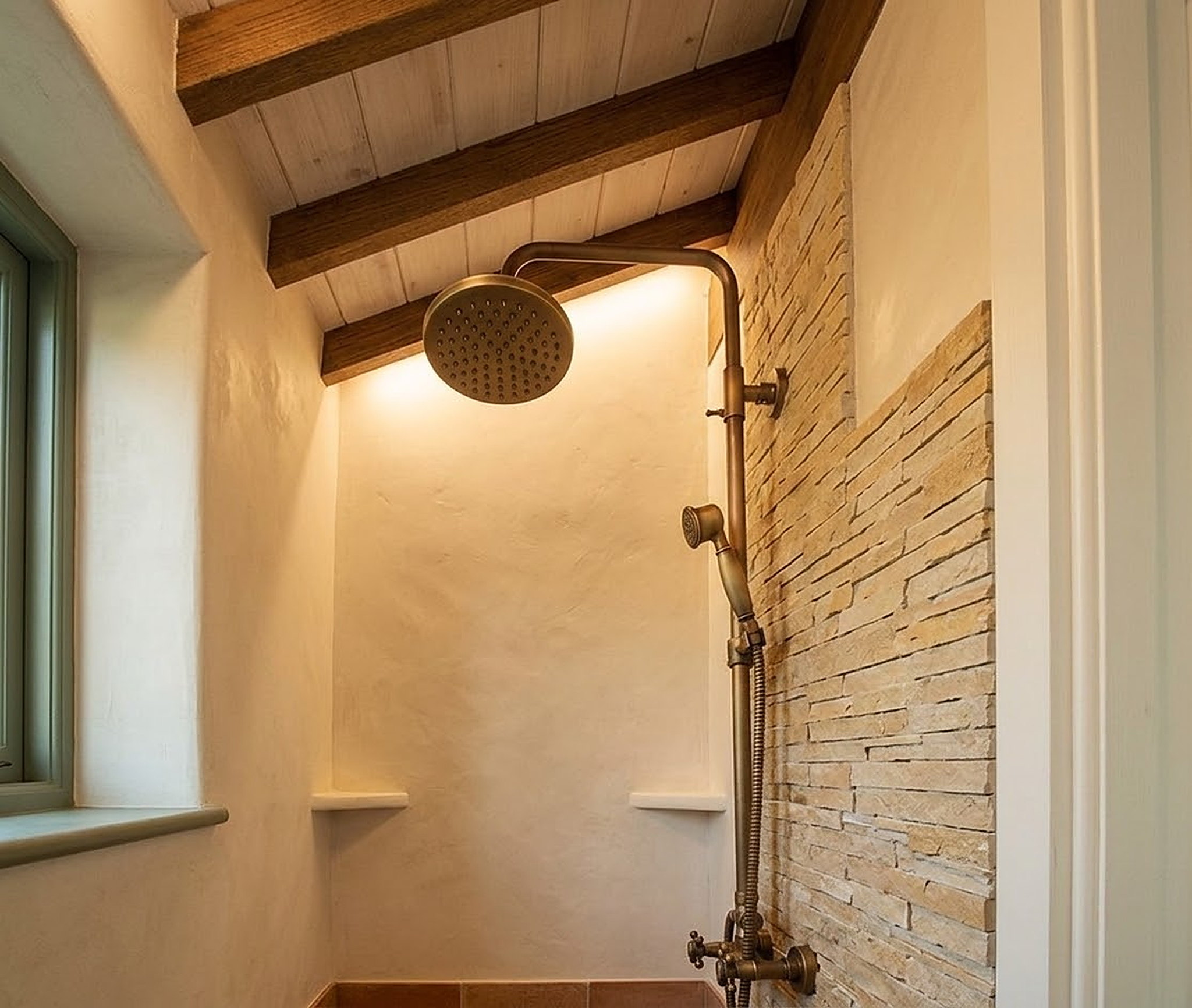The shower in Residence 21ft, a brass rain head against a stacked stone wall
